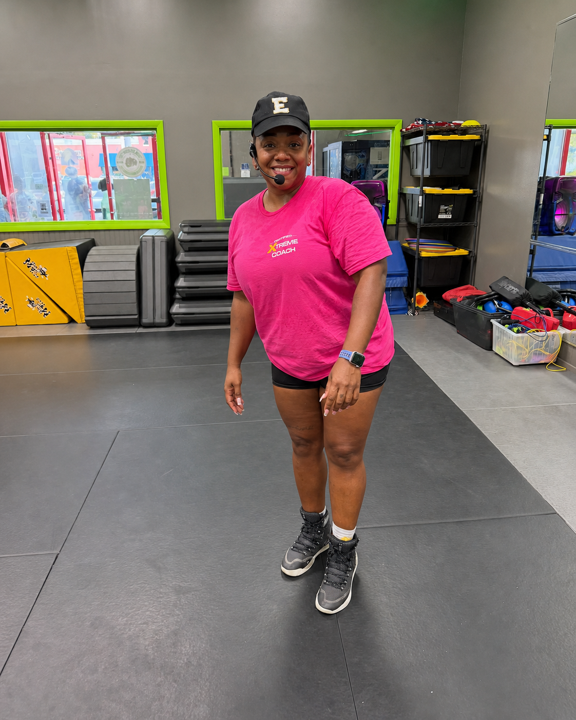 Coach Erika standing in the studio in her pink Xtreme Hip Hop coach shirt and headset
